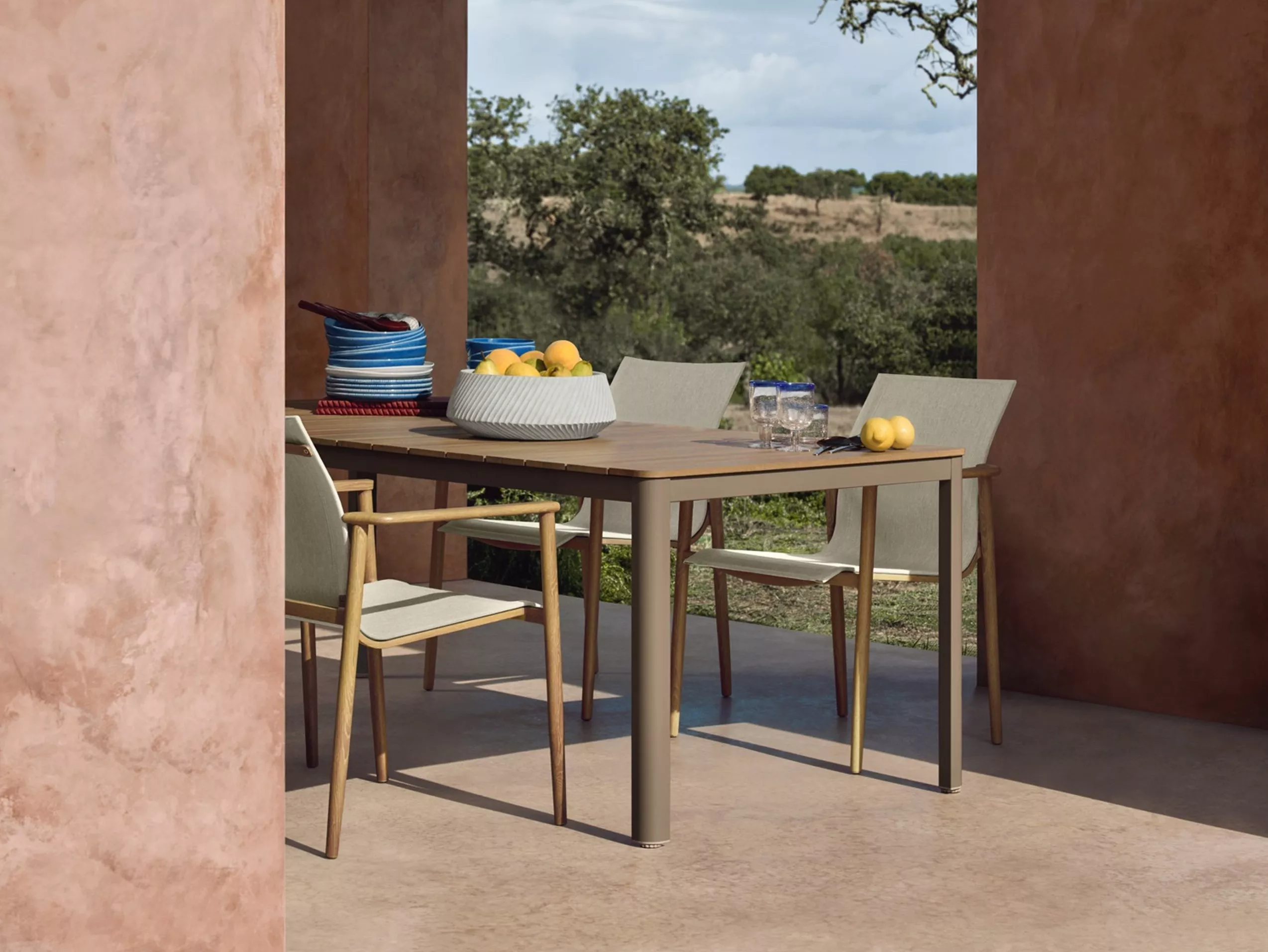 Modern outdoor dining table set by a swimming pool, with chairs, candles, plates and colourful glassware on patio