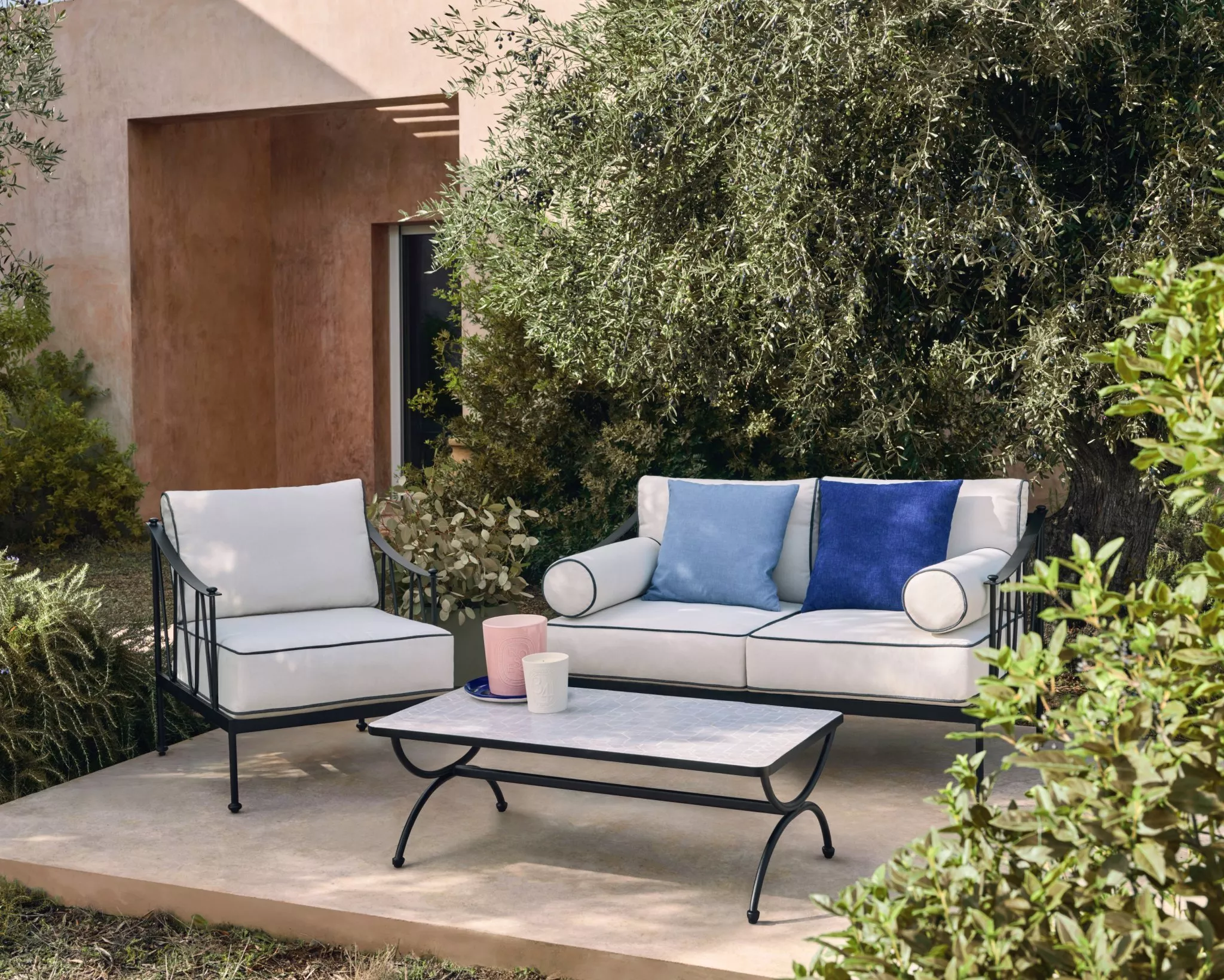Elegant outdoor patio furniture set with white sofa and chair, blue cushions and coffee table by olive tree