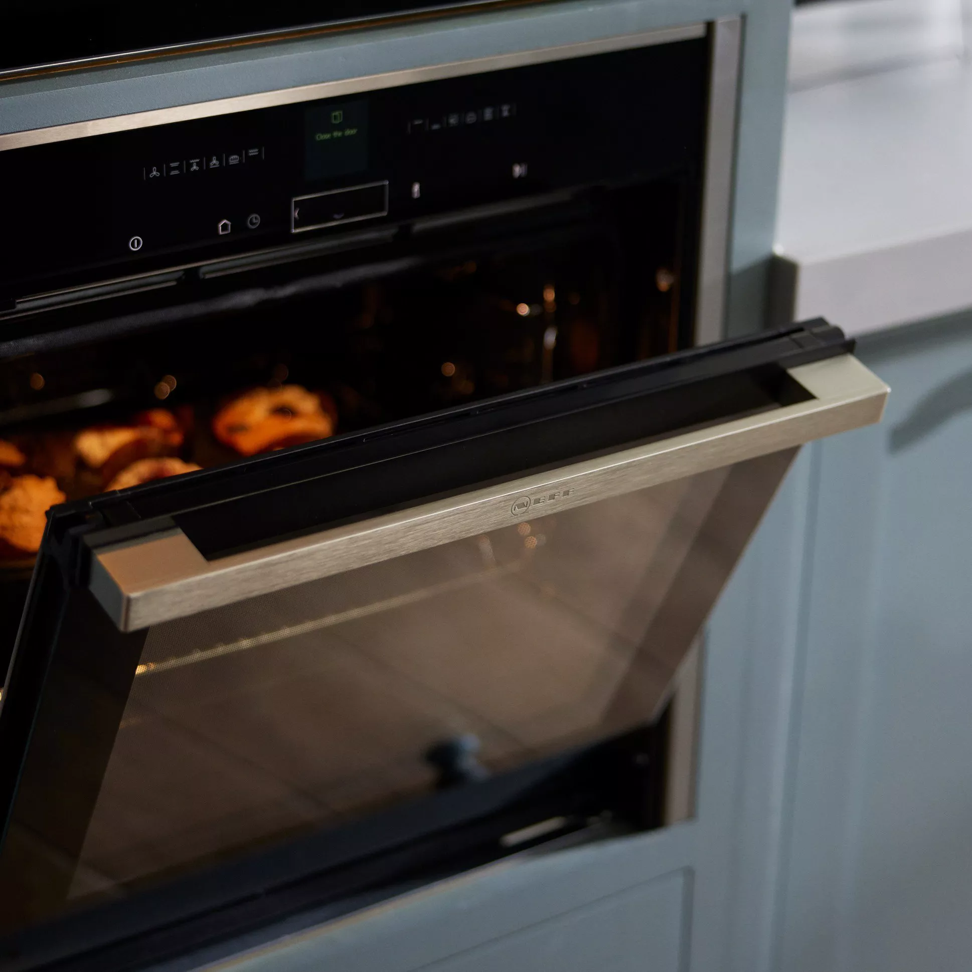 Modern oven with digital controls, partially open, revealing freshly baked goods inside. Sleek kitchen design.