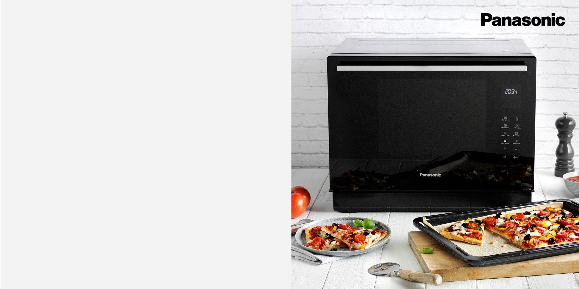 A black Panasonic microwave oven on a white table, surrounded by food ingredients.