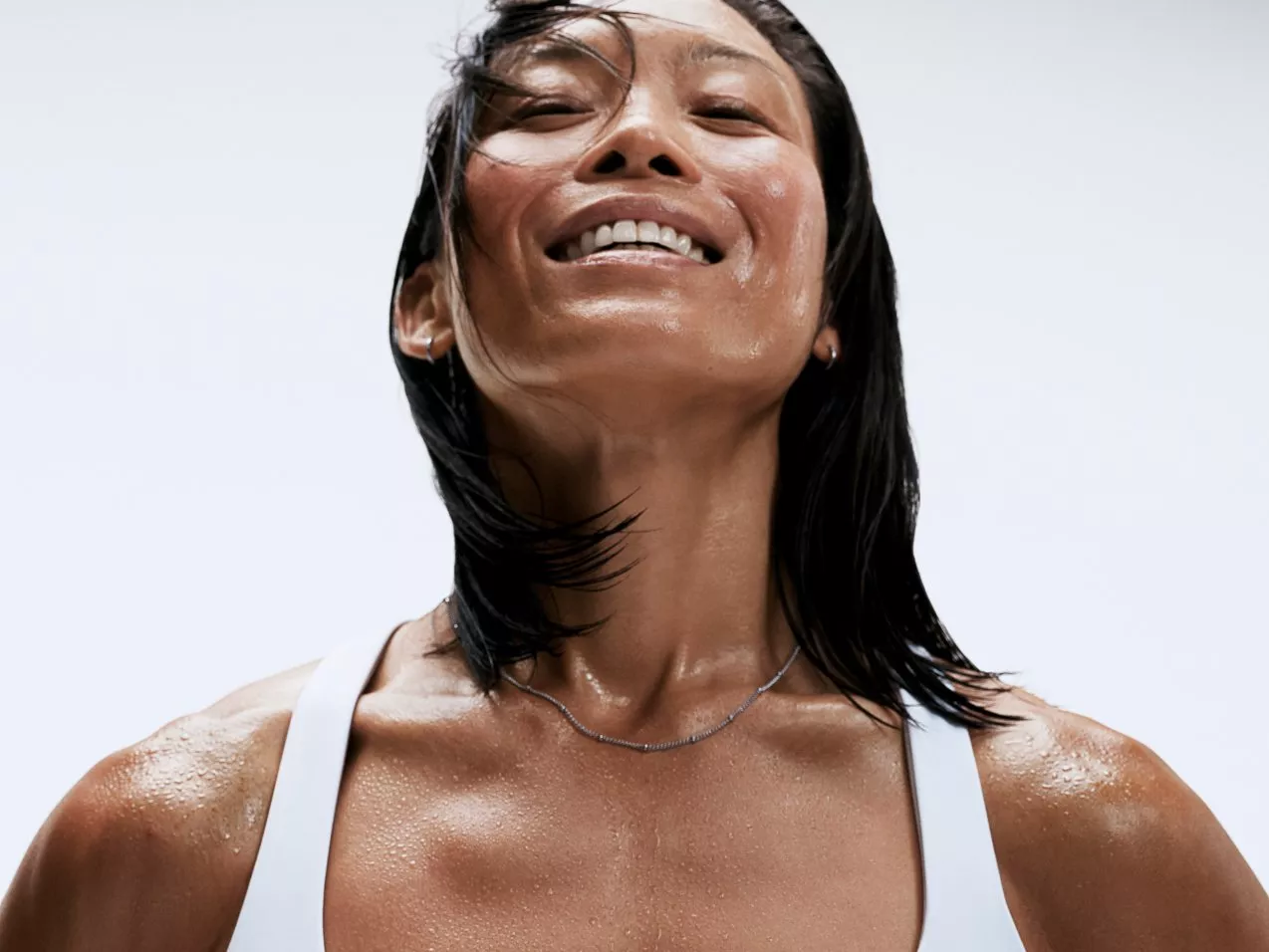 a woman head back eyes closed and a bit sweaty in a white gym top