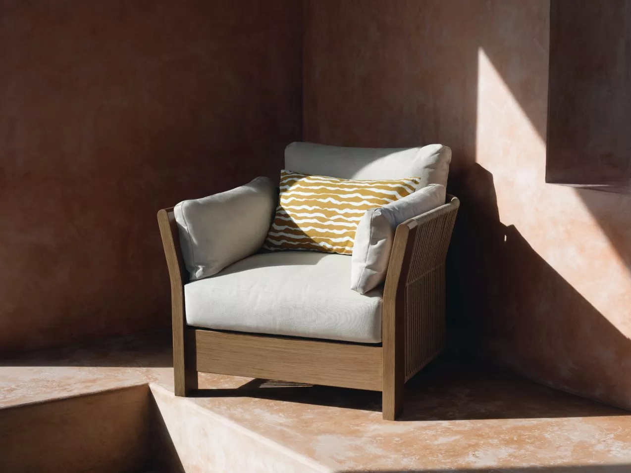 Modern wooden armchair with beige cushions and yellow patterned pillow in sunlit minimalist interior corner
