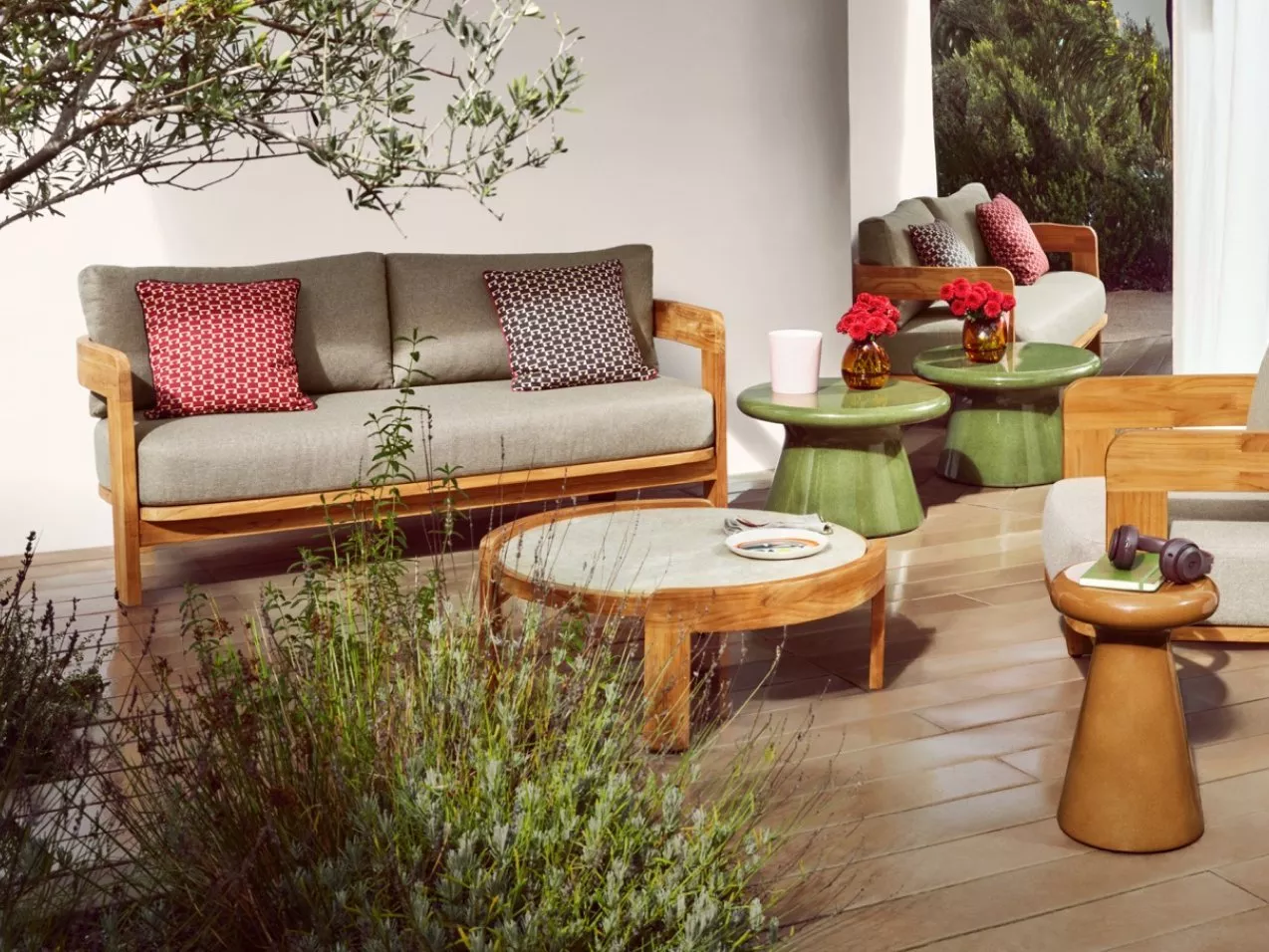 Modern outdoor patio seating with wooden sofas, grey cushions, green side tables and a round coffee table in sunlight