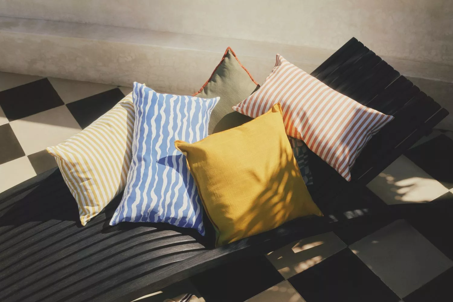 Colourful striped outdoor cushion covers on black sun lounger, sunny patio with checkerboard tiles