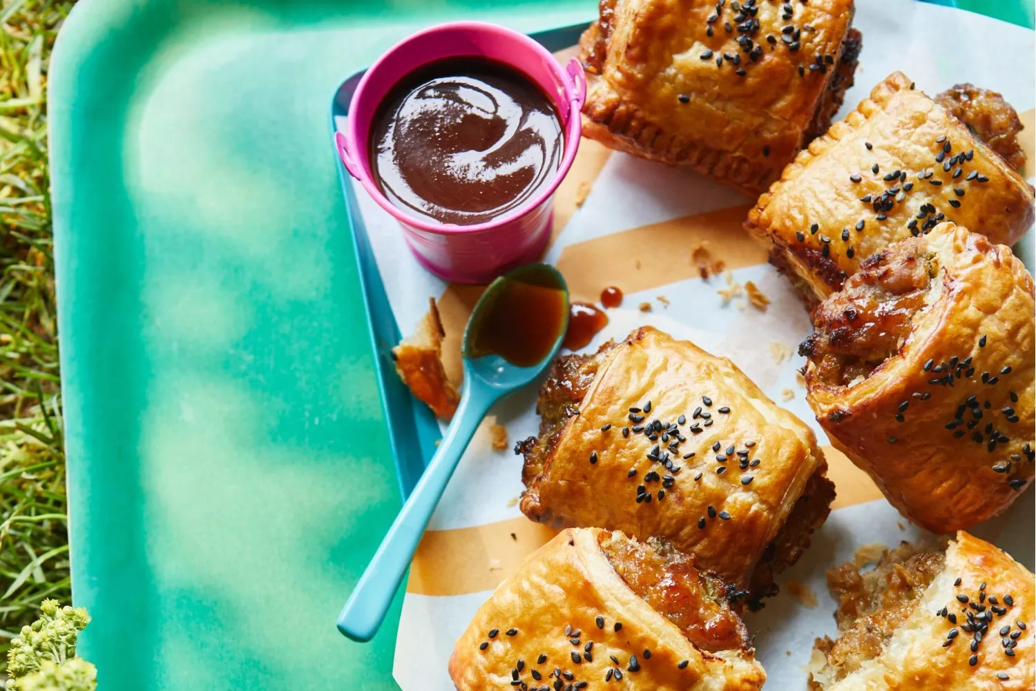 Sausage rolls with black sesame seeds, served with barbecue sauce dip on a picnic tray outdoors