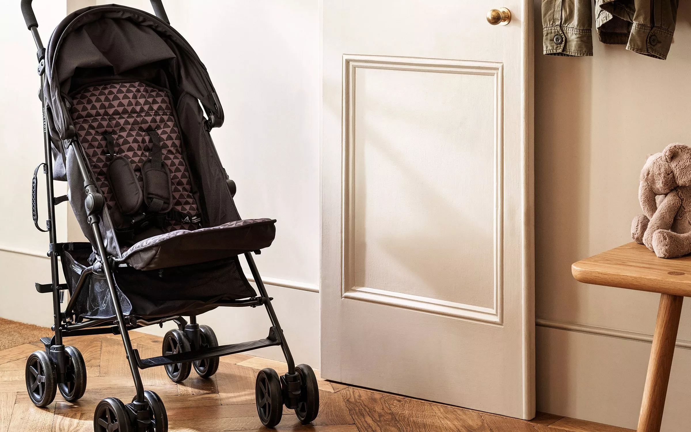 Lightweight baby stroller by white door in hallway, with wooden bench and soft teddy toy beside it