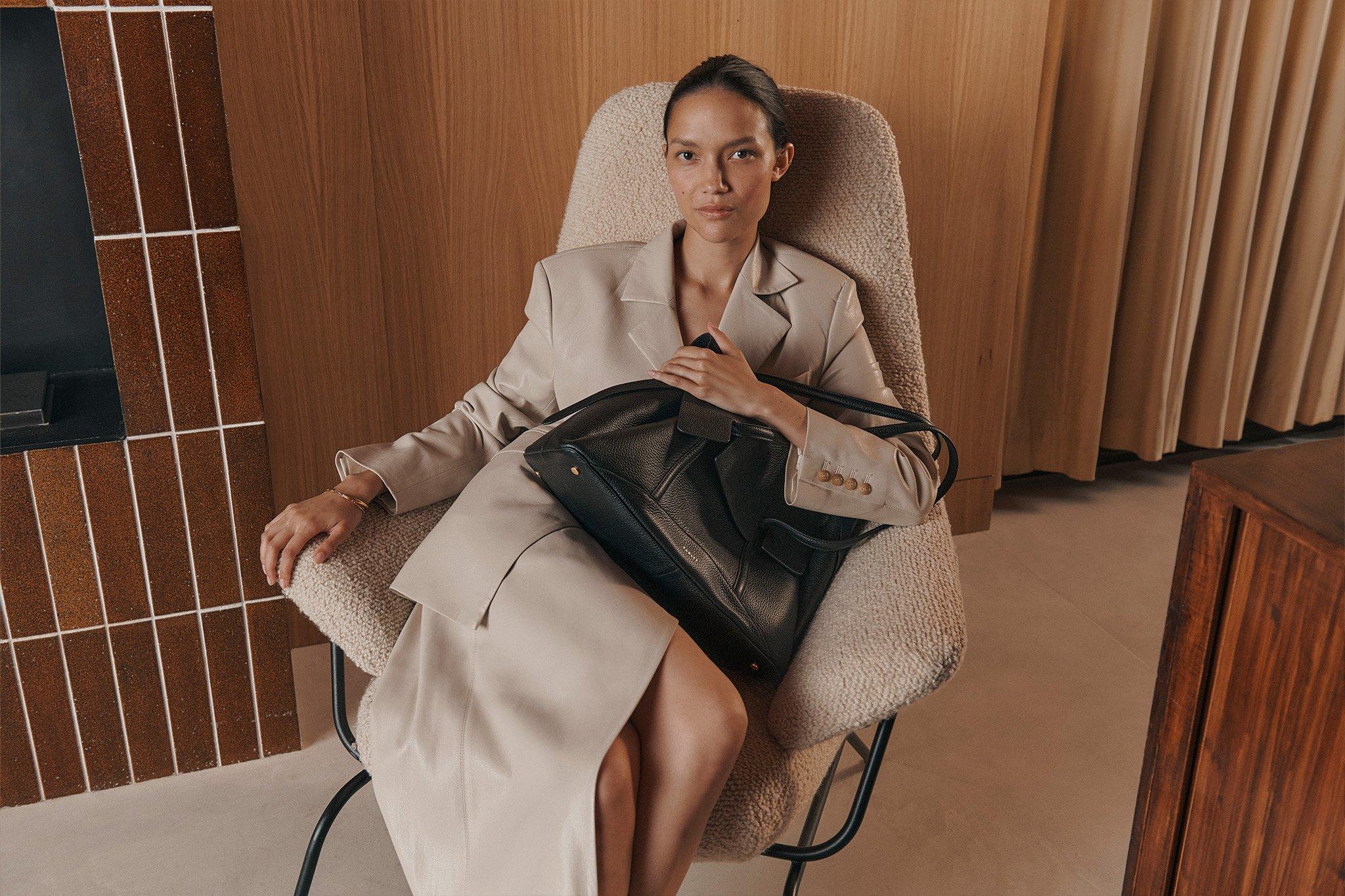 Woman seated holding black Chancery shoulder bag