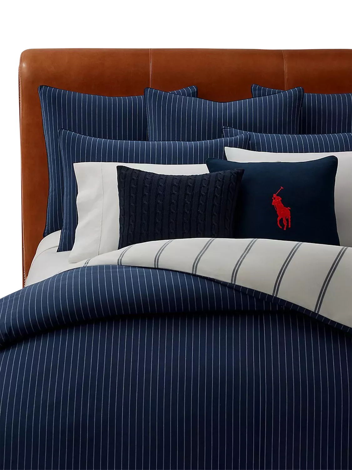 Navy pinstripe bedding set with striped duvet, cushions and tan leather headboard, modern bedroom style