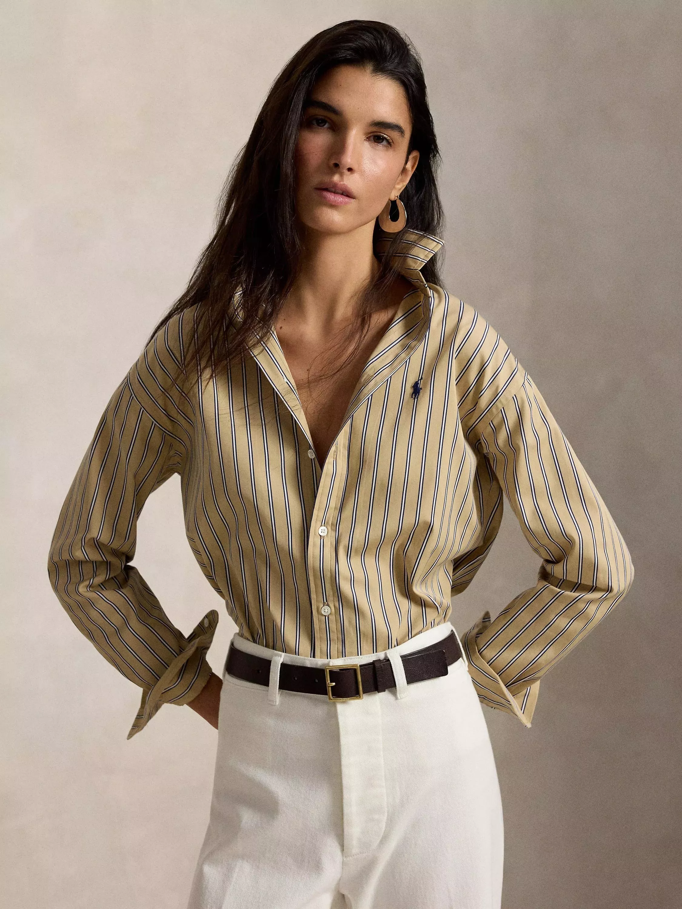Fashion portrait of a woman wearing a striped button-down shirt with white trousers and belt