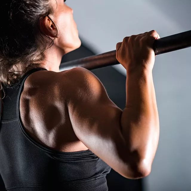 Close-up of woman doing pull-up on bar in gym, showing strong back and arm muscles during workout