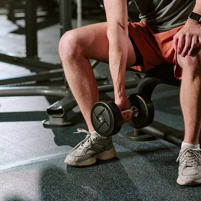 Person doing seated dumbbell curl in gym, close-up of legs and hand lifting weight for strength training