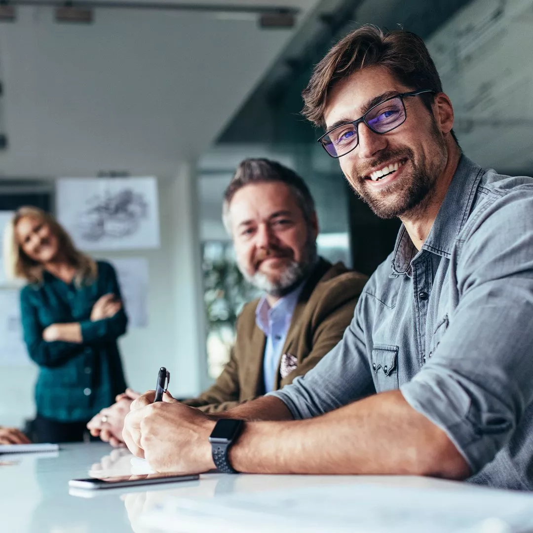 Business meeting scene with individuals engaged in discussion. Papers and a pen are on the table.