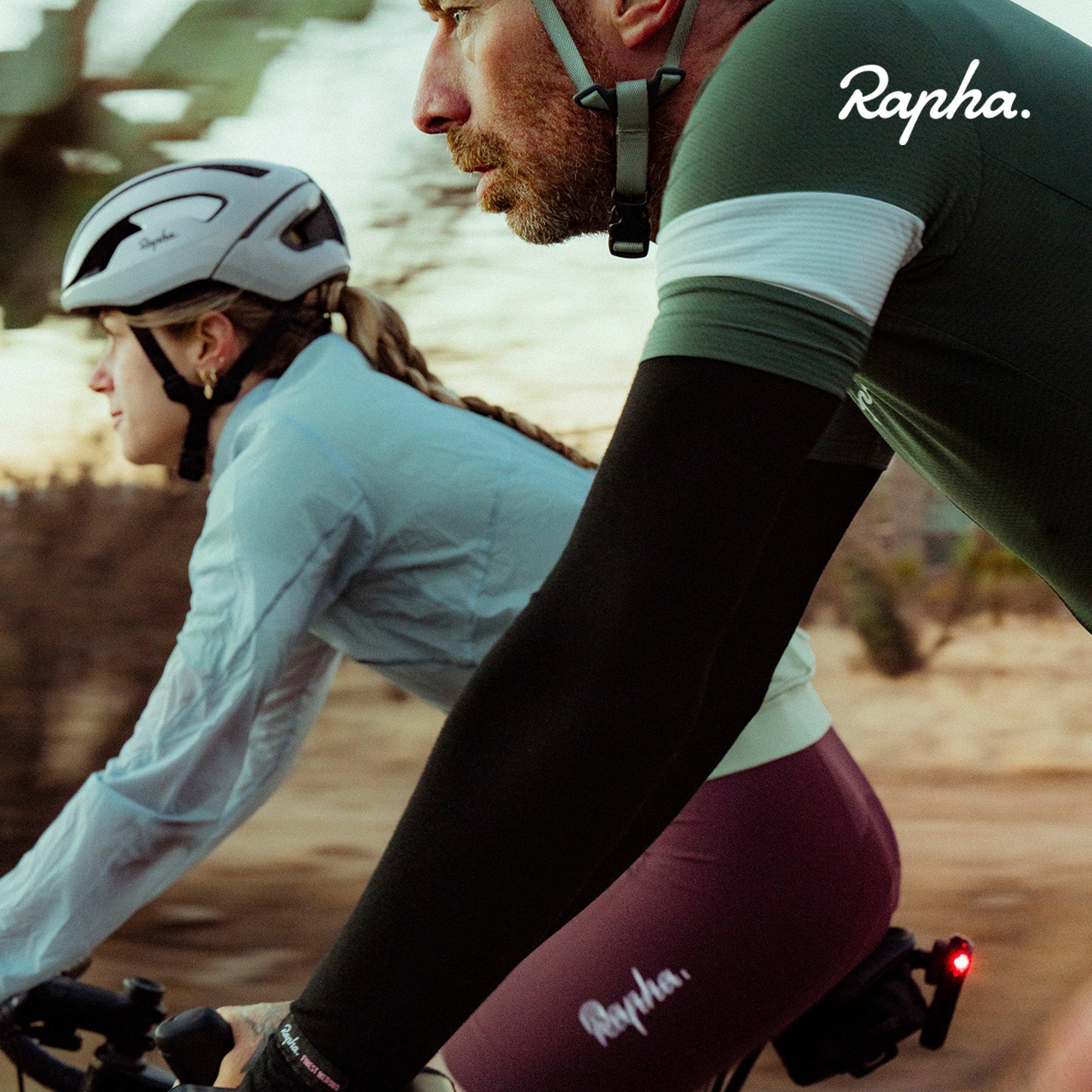two cyclists riding side by side wearing helmets and cycling apparel from the brand Rapha
