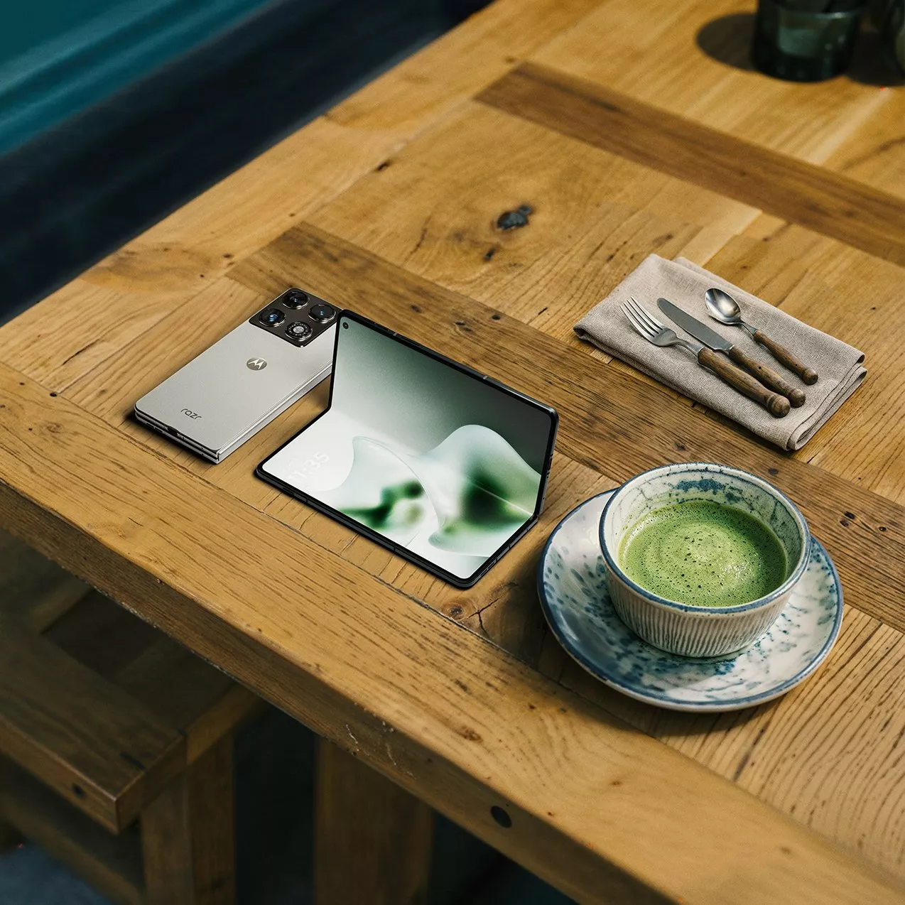 Foldable smartphone and small tablet on wooden café table beside matcha latte and cutlery set