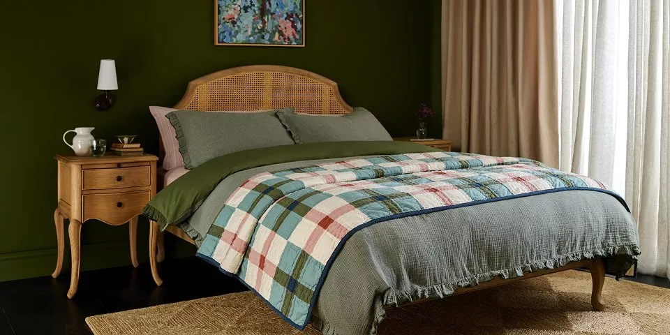 A bed with a curved, woven cane headboard is styled with layered linens.