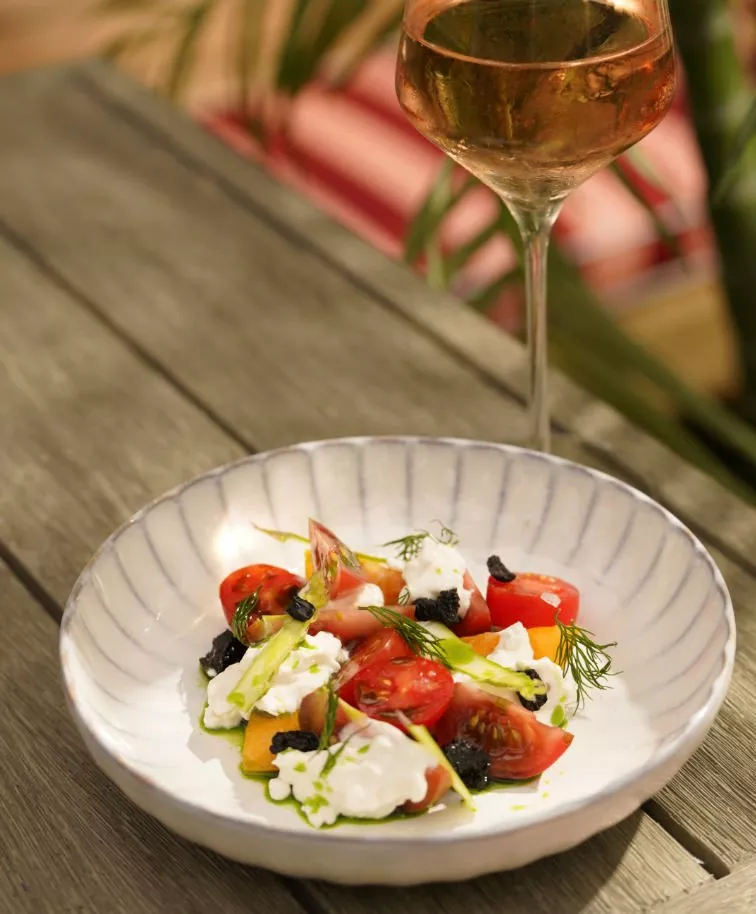 Fresh salad with tomatoes, cheese, and herbs in a ceramic bowl, on a wooden table.