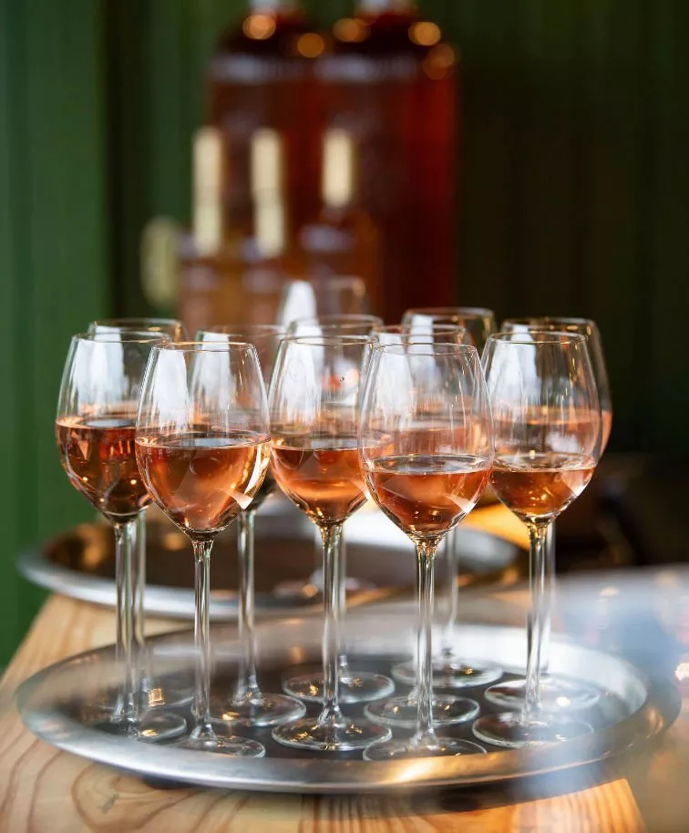 Elegant glasses of rosé wine on a silver tray, set against a blurred background of wine bottles.