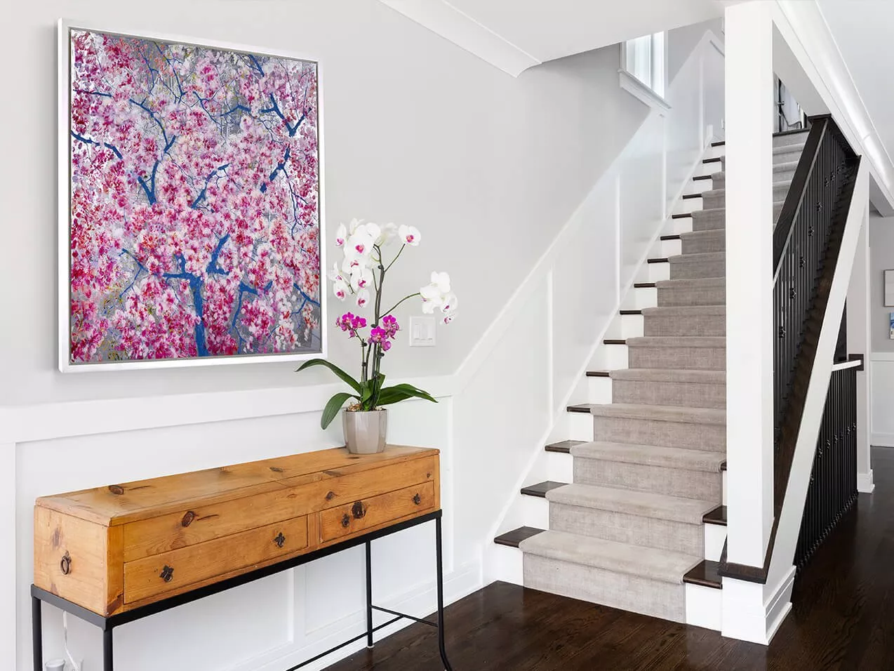 Modern hallway with staircase, wooden console table, orchid plant and large pink floral wall art print.