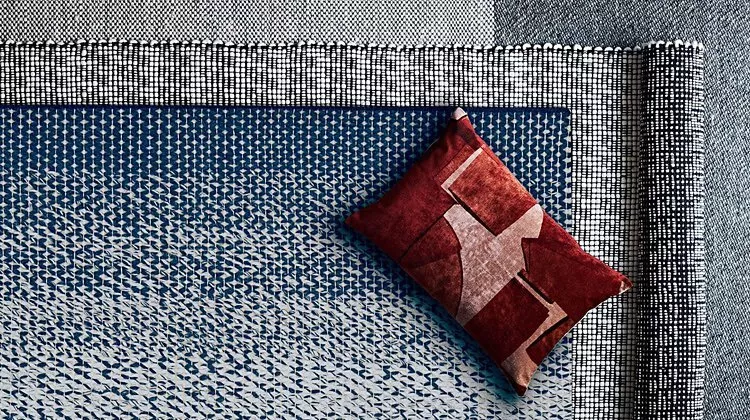 Geometric-patterned rugs in blue and grey tones, with a red cushion featuring abstract designs on top.