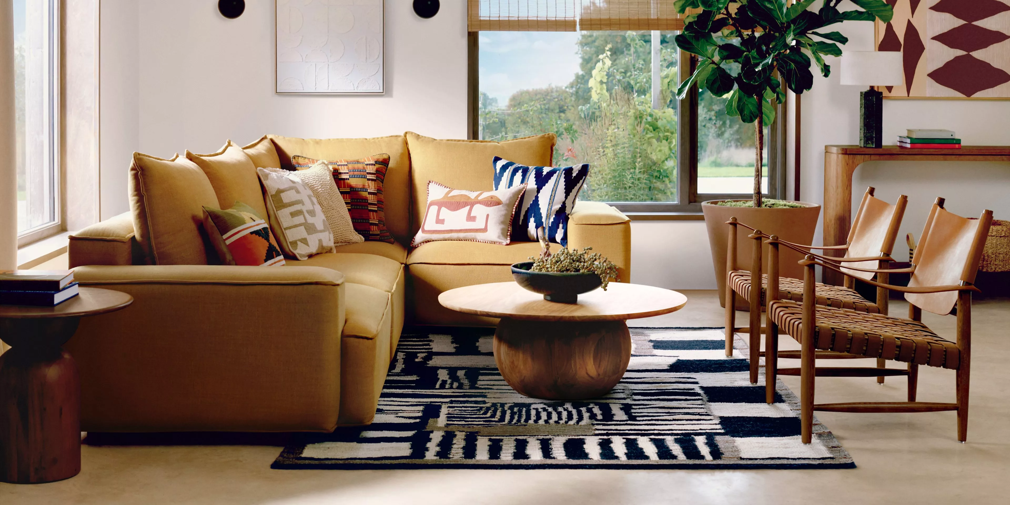 Cosy living room with a mustard sofa, patterned cushions, modern chairs, and a large plant by the window.