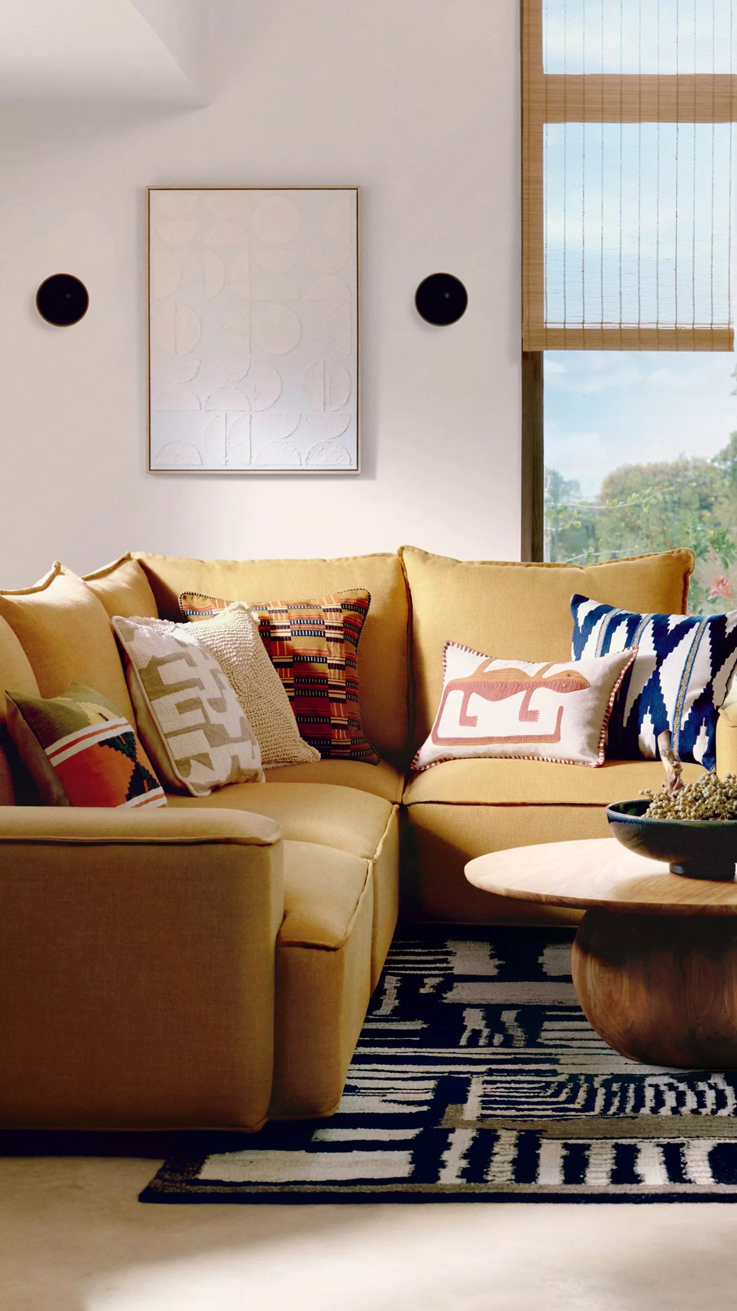 Cosy living room with a mustard sectional sofa adorned with patterned cushions, a round wooden table, and wall art.