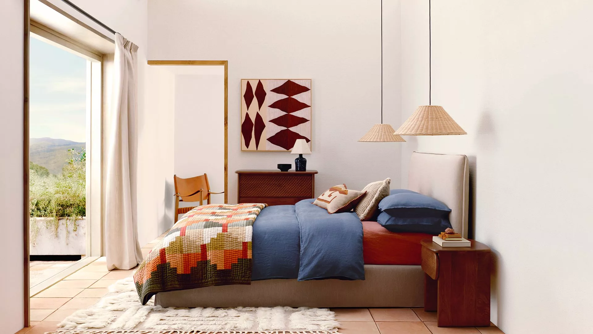 Stylish bedroom with a colourful quilt, blue bedding, and natural light from an open window with scenic views.