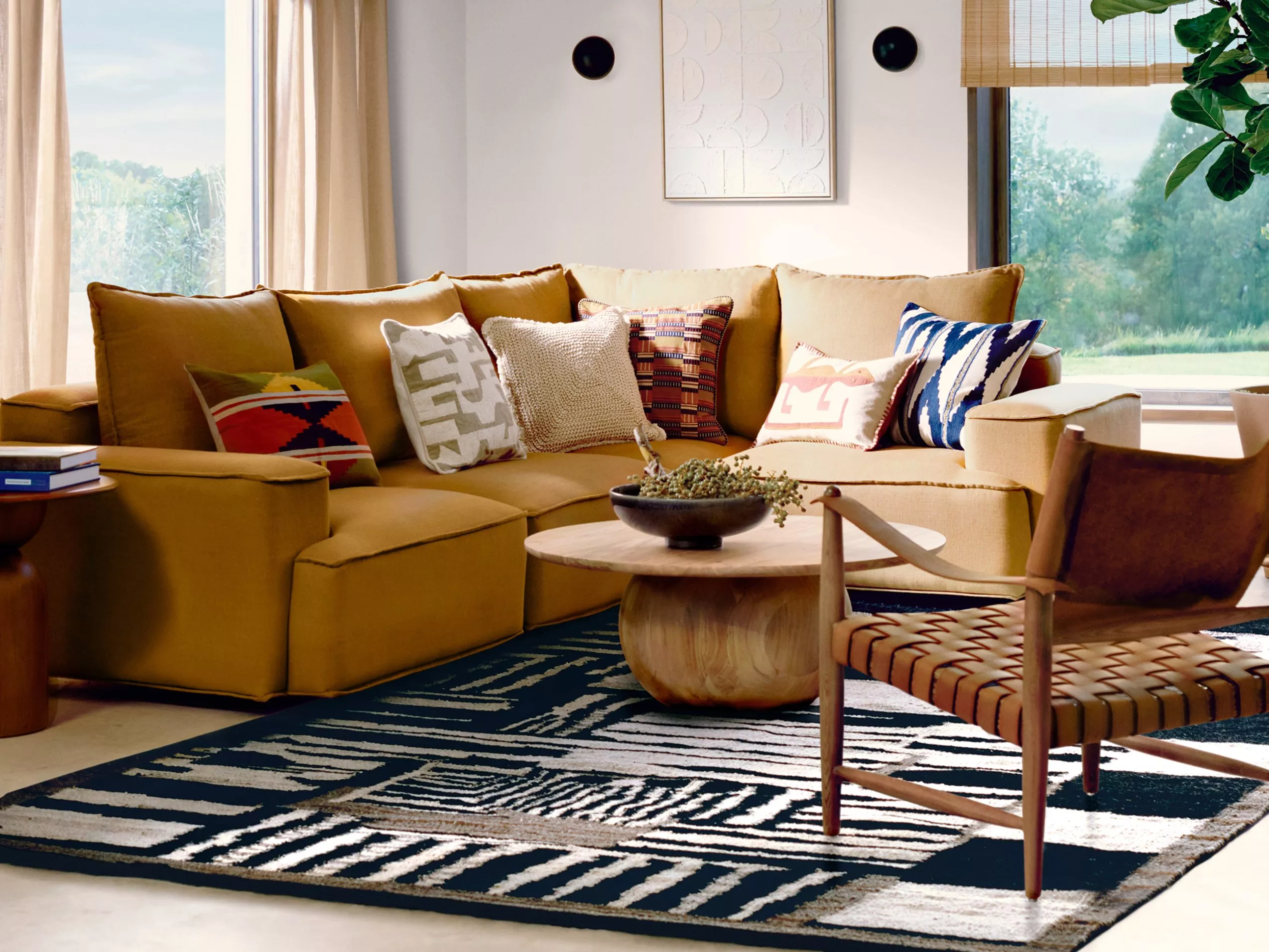 A stylish living room with a mustard sectional sofa, patterned cushions, a wooden coffee table, and a woven chair.
