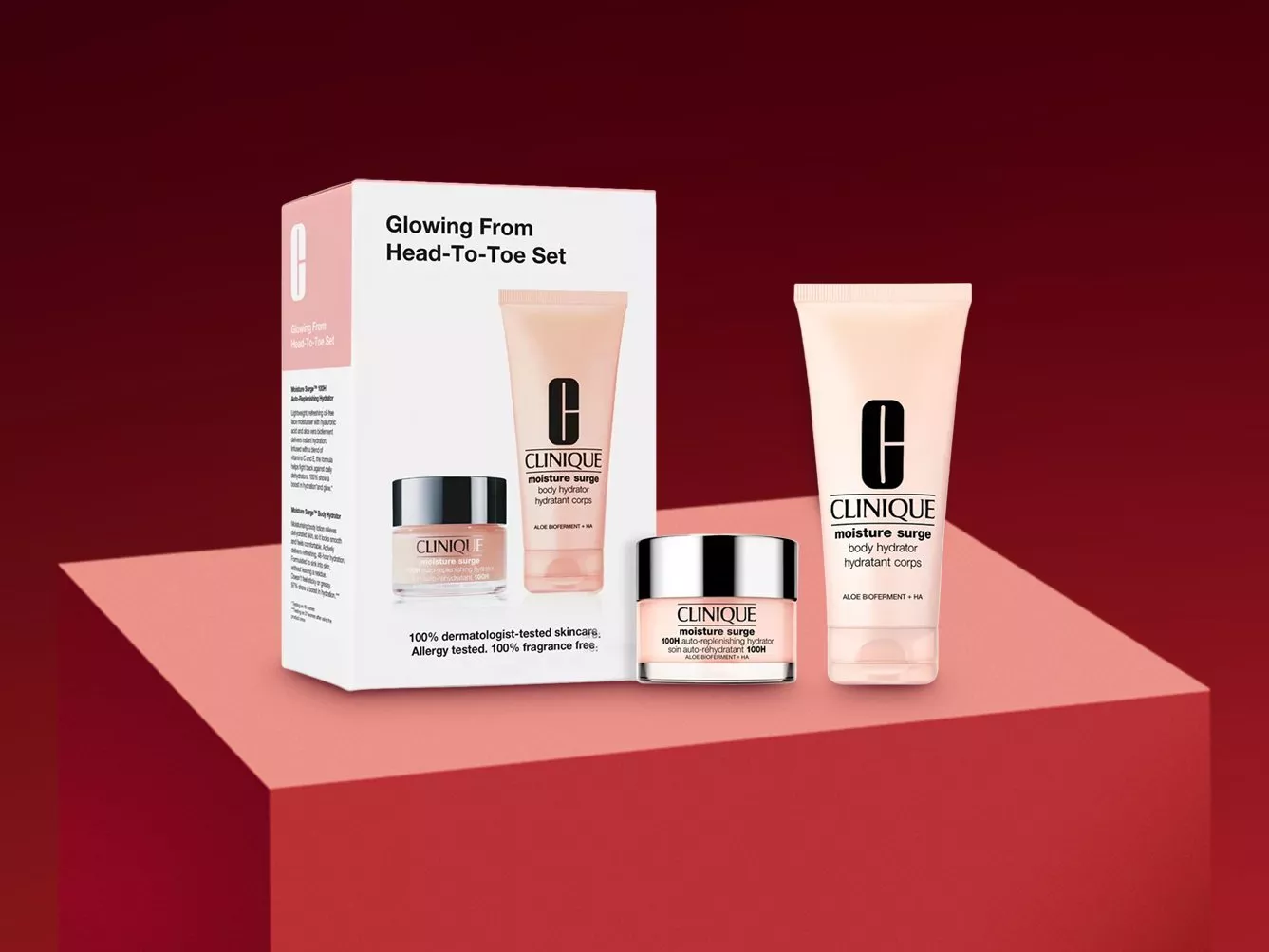 Clinique Glowing From Head-To-Toe Set with Moisture Surge cream jar and body hydrator, boxed on pink plinth.