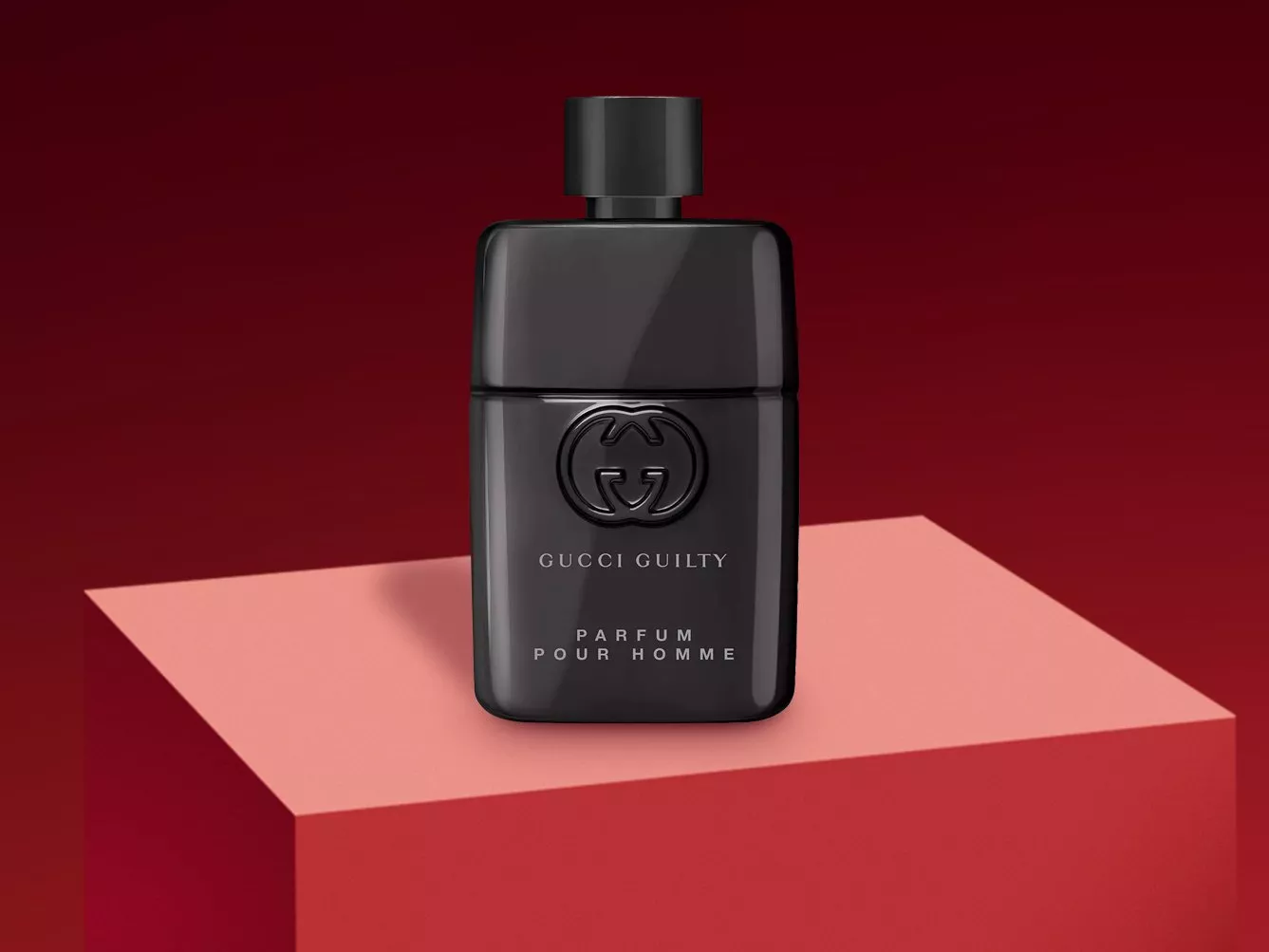 Gucci Guilty Parfum Pour Homme black fragrance bottle on pink plinth, red background, luxury men’s scent product shot