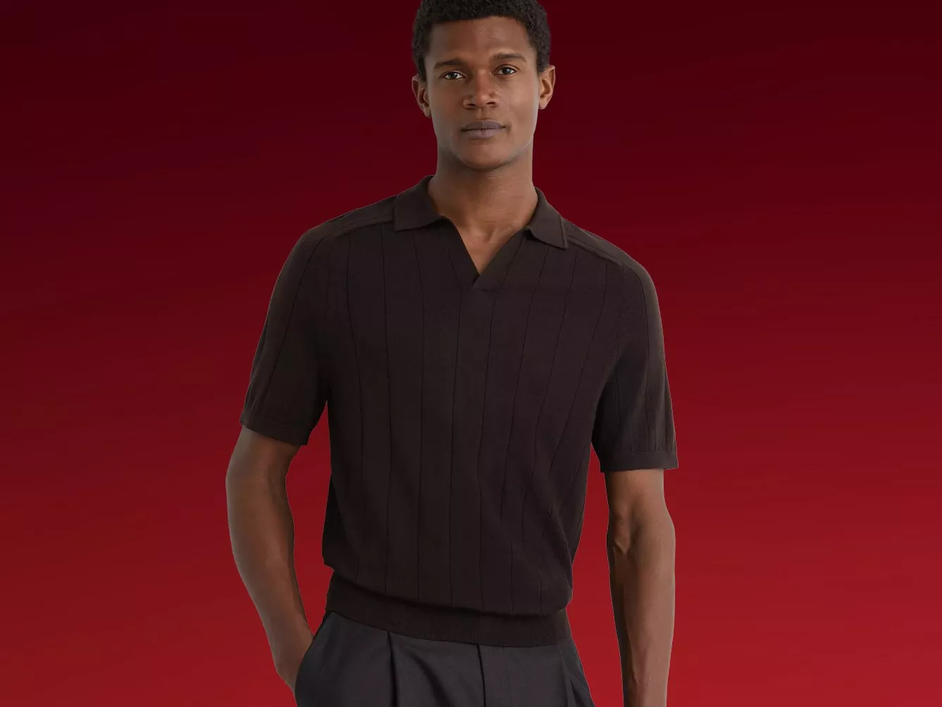 Male model wearing a dark brown knitted polo shirt, smart casual menswear style, posed against a burgundy backdrop