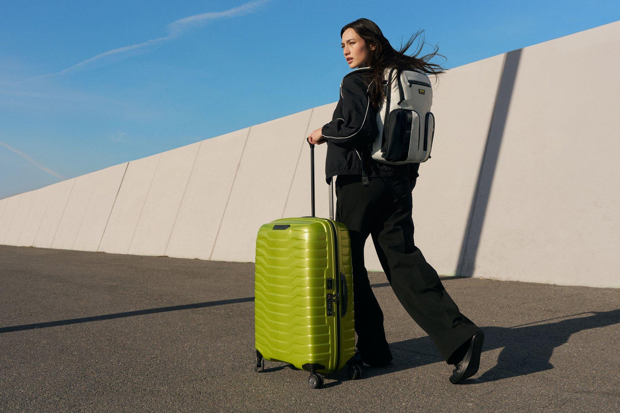 Image of a woman pushing a samsonite suitcase down the road in bright sunshine