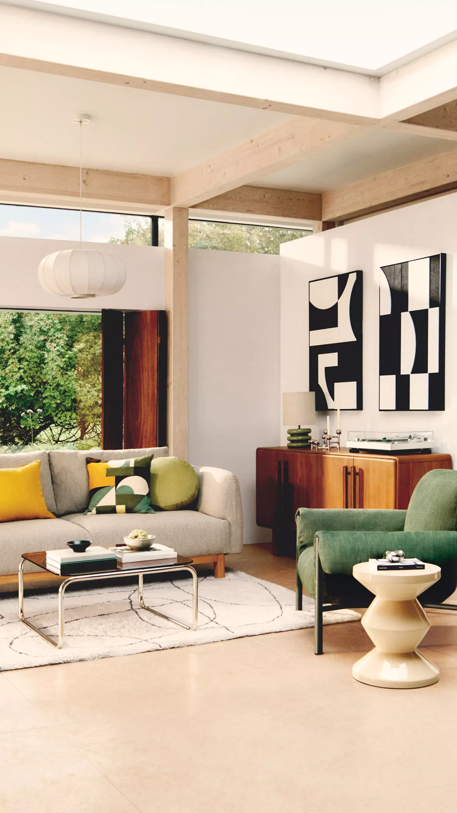 Modern living room with stylish decor, featuring a grey sofa, geometric art, and vibrant cushions. Large windows add light.