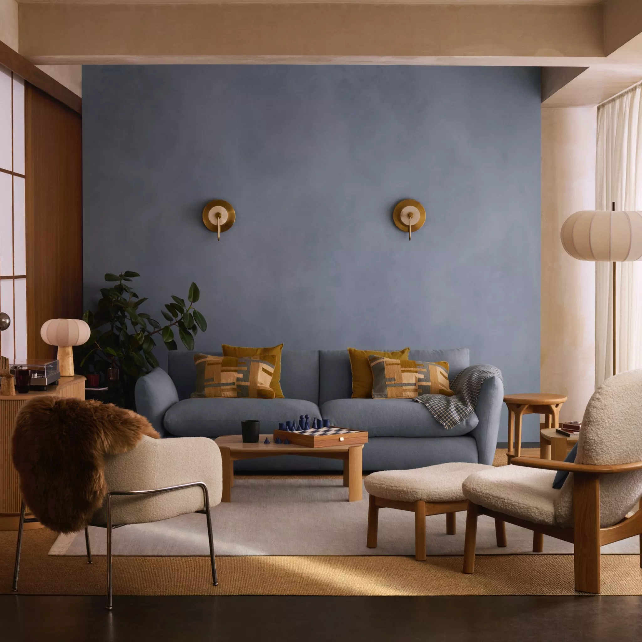 Modern living room with blue sofa, brass wall lights, timber furniture and cosy neutral armchairs.