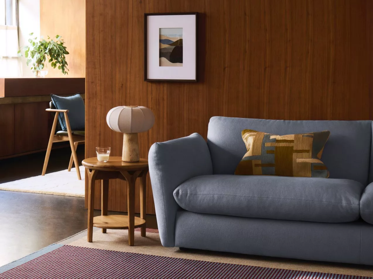 Mid-century modern living room with blue sofa, wooden wall panelling, side table lamp and framed artwork