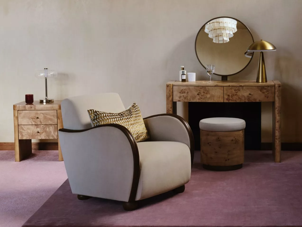Modern lounge chair with patterned cushion beside burl wood dressing table, round mirror and brass lamp.