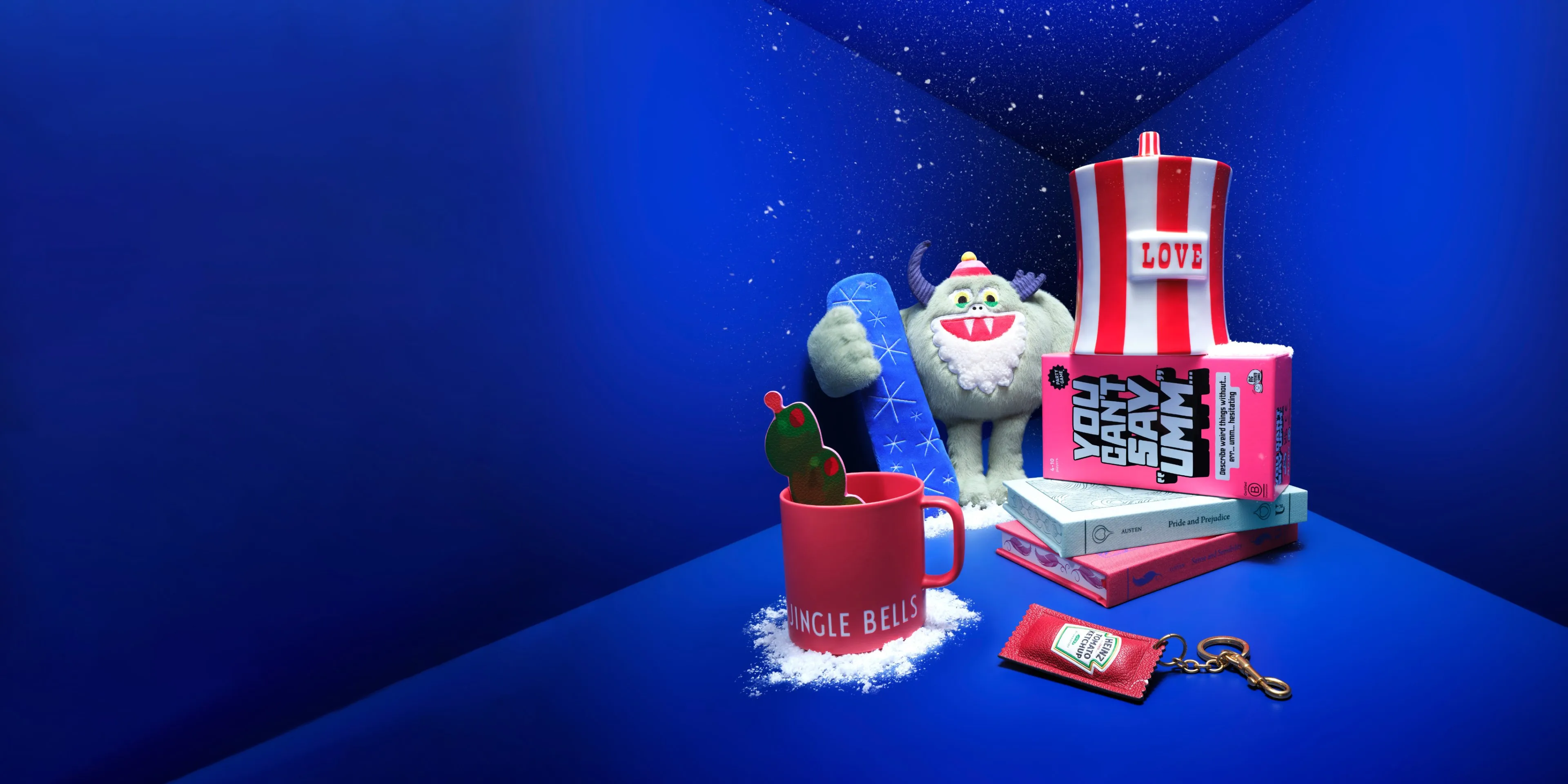 Festive blue still life with plush yeti, Jingle Bells mug, books, love cup and ketchup keyring in snow