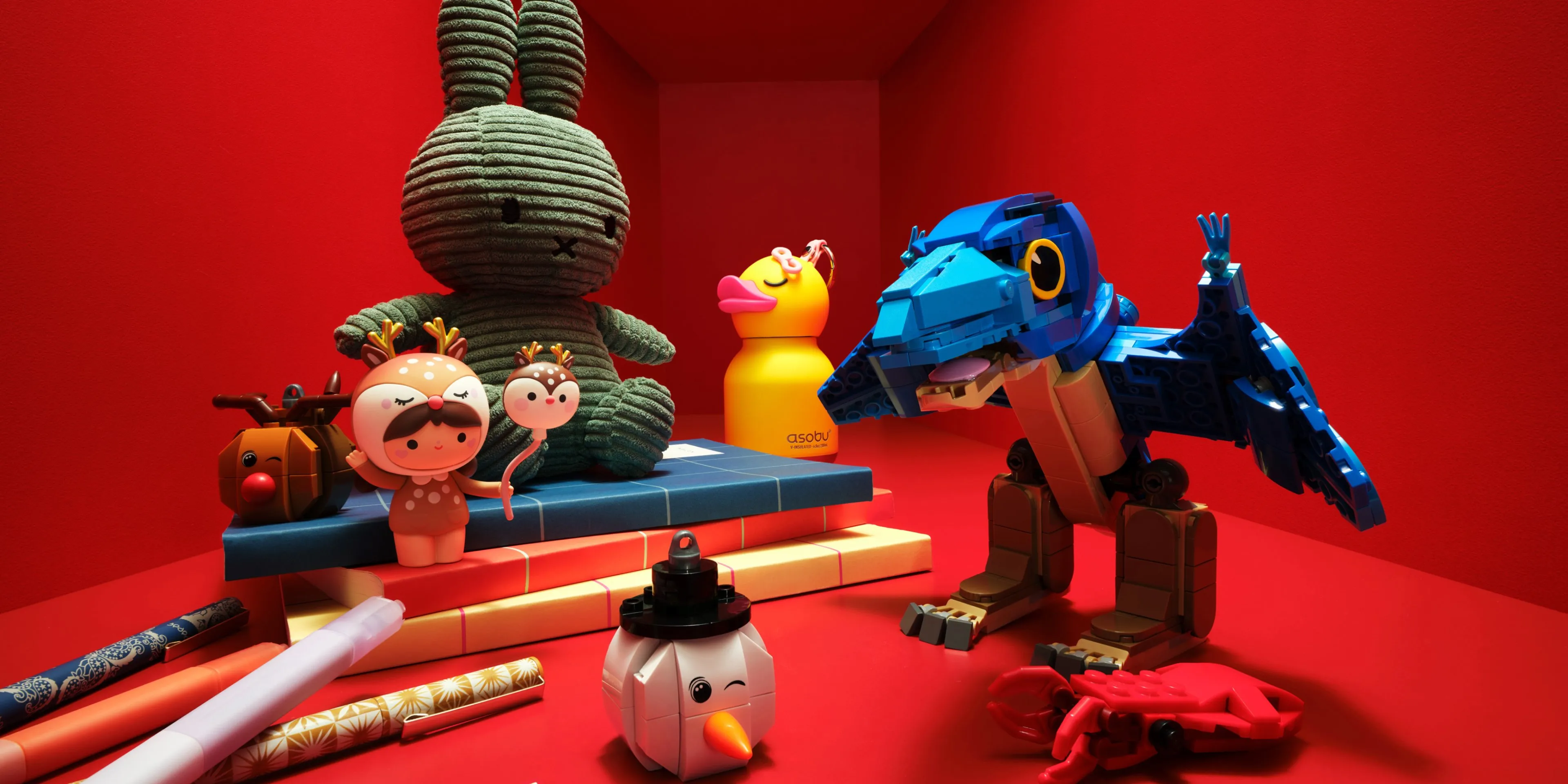 Colourful toy display on red shelf with blue LEGO bird, plush bunny, duck bottle, snowman and crab figures