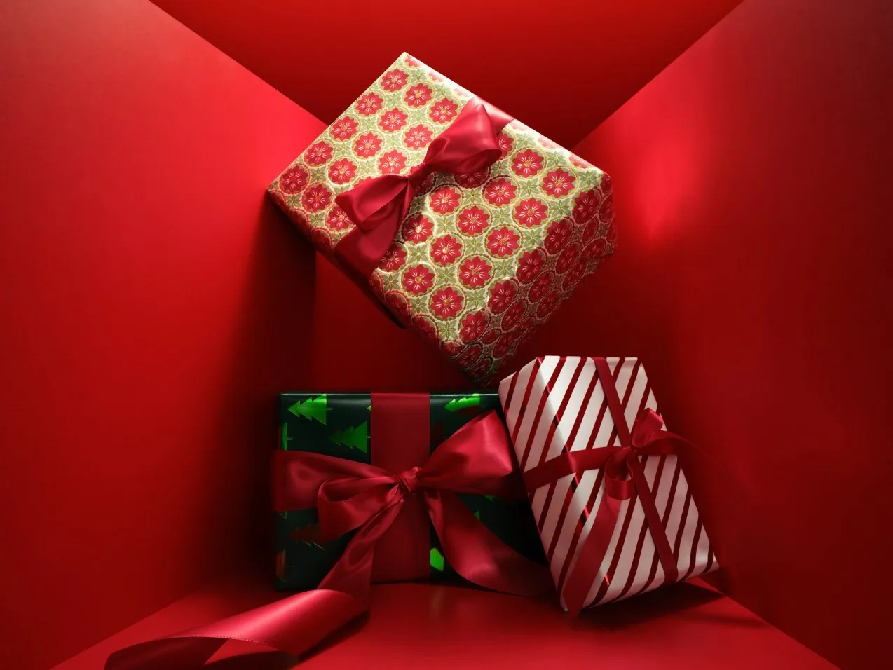 Festive Christmas gift boxes with red ribbon bows on a bright red background, holiday wrapping paper assortment