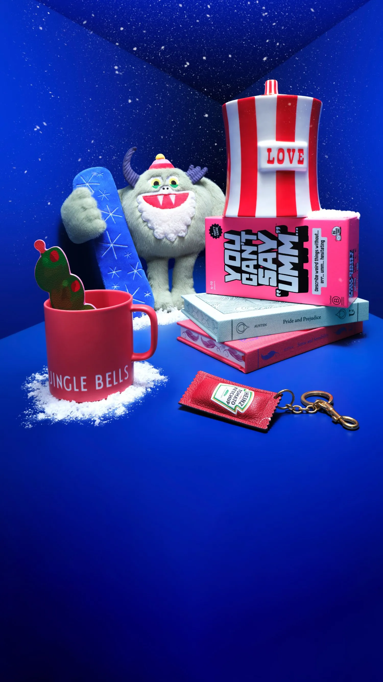 Festive flat lay with snowy yeti toy, books, LOVE striped cup, Jingle Bells mug and ketchup keyring on blue background
