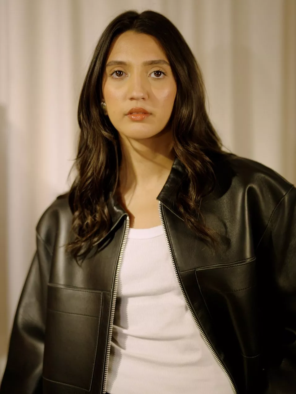 Portrait of Sapna Rao in a black leather jacket and white top, studio fashion photo with soft lighting.