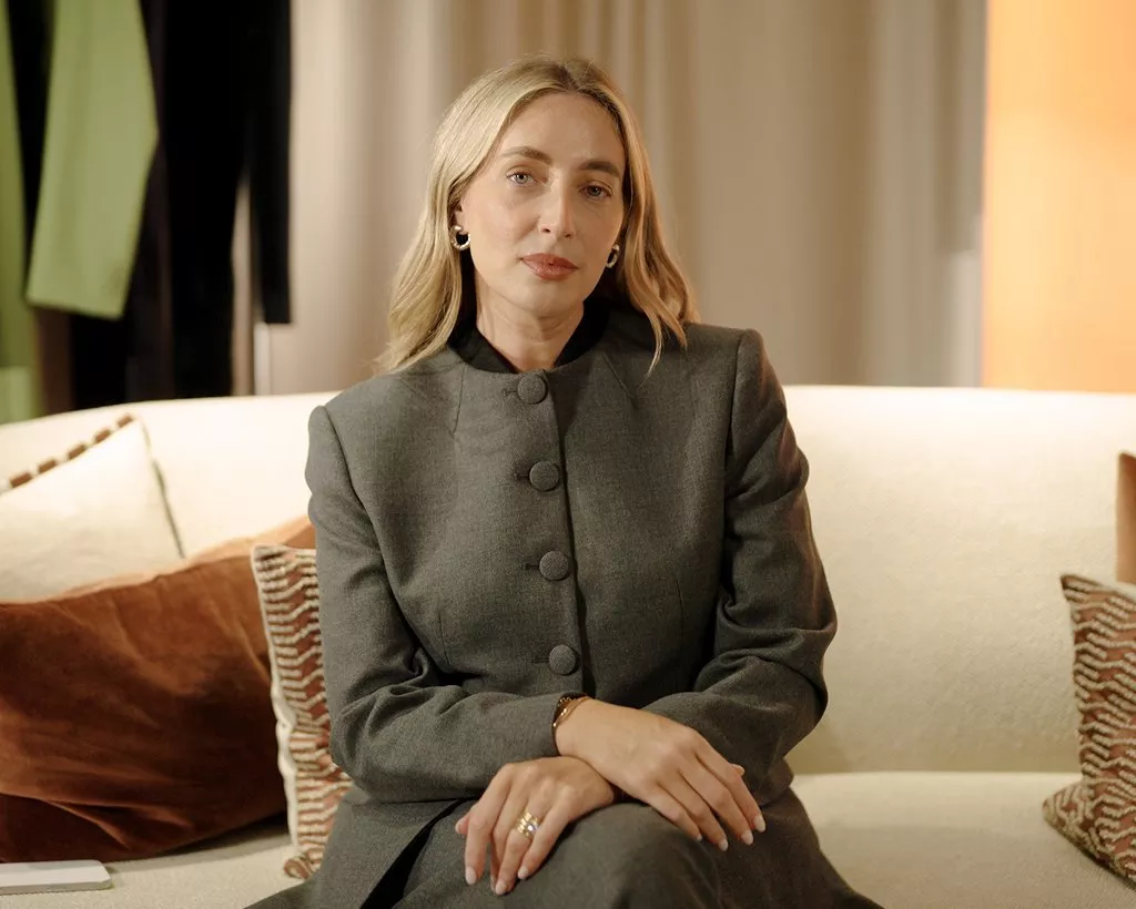 Portrait of a blonde woman in a grey suit sitting on a sofa in a stylish living room, warm lighting