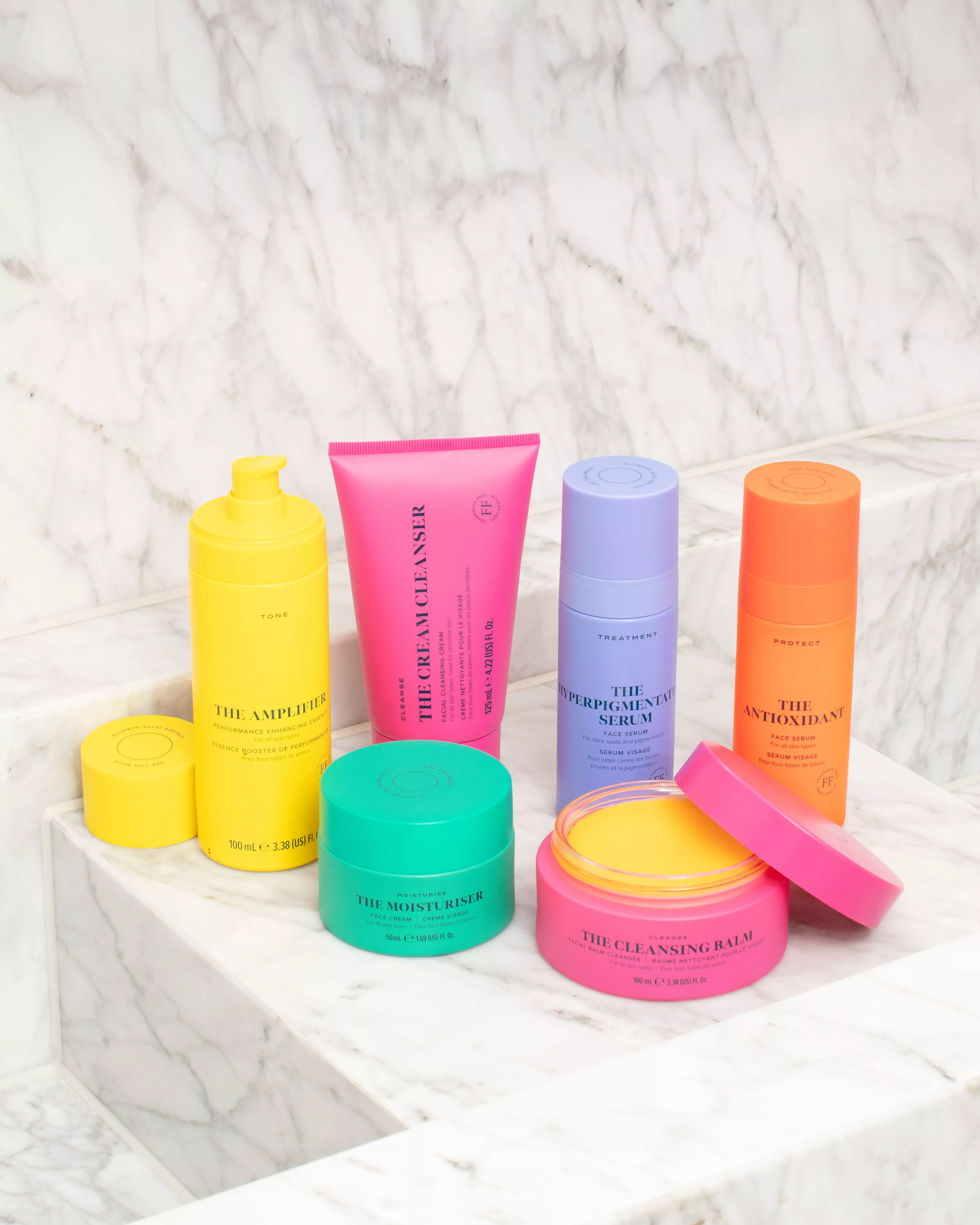 Brightly coloured skincare products arranged on marble steps, each with distinct packaging design.