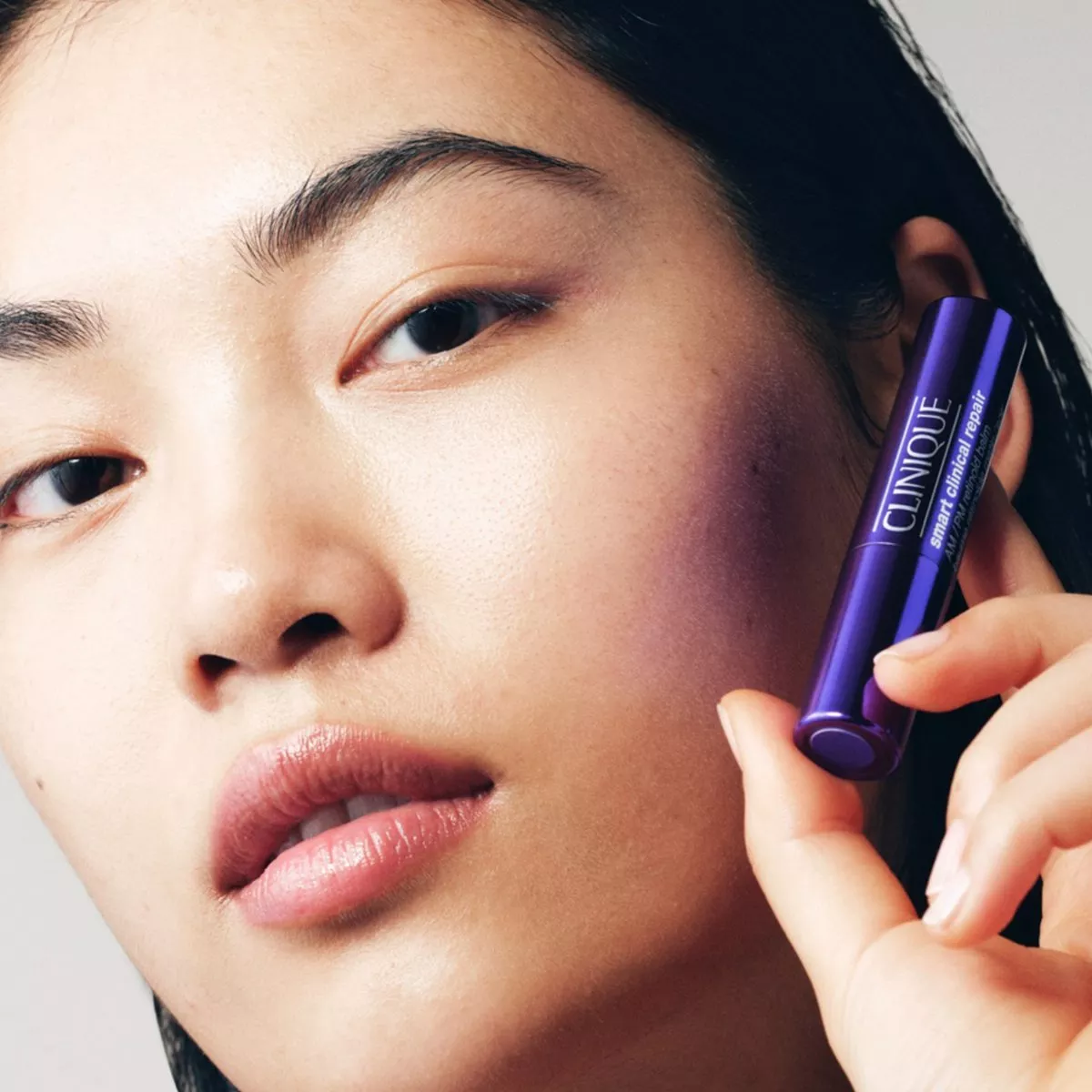 close up of woman holding a Clinique retinoid balm next to her face