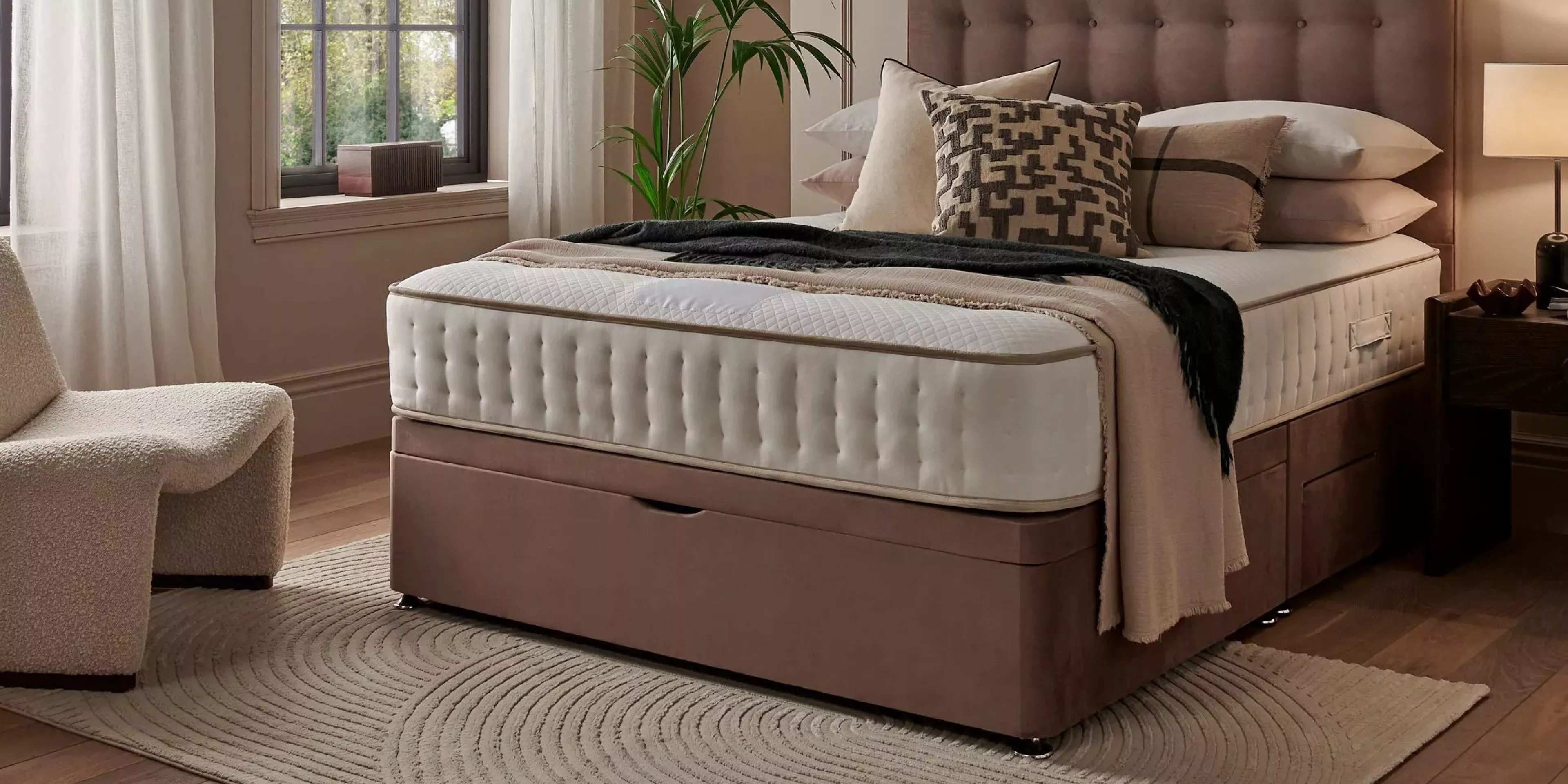 Luxury upholstered ottoman storage bed with tufted mattress, neutral bedding and bedside lamp in cosy bedroom.