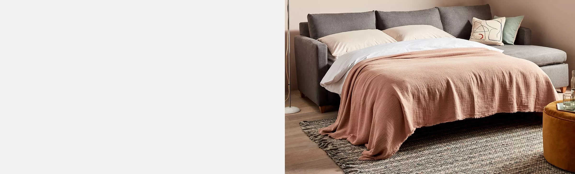  A grey sofa bed made up with neutral pillows and duvet and a pink throw