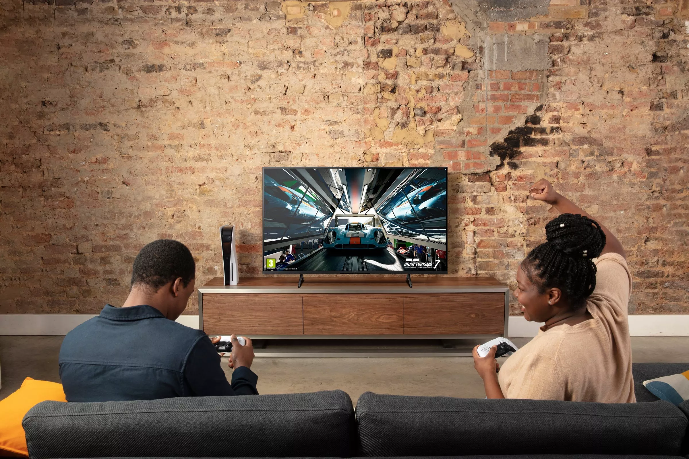 Two people playing PlayStation on a big TV 