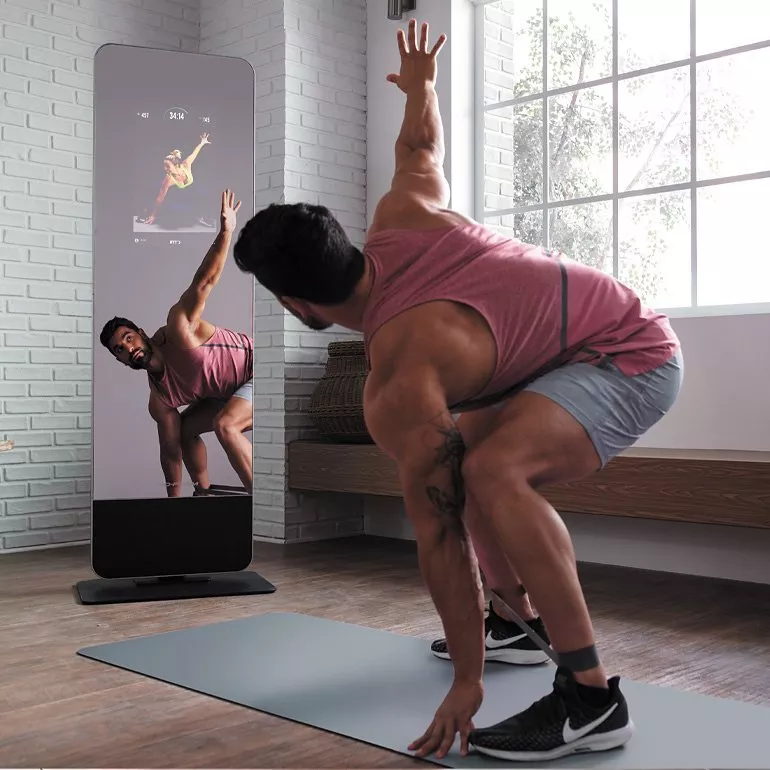 Man stretching on yoga mat using smart fitness mirror for home workout in bright modern living room.