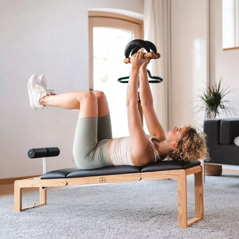 Woman doing core workout on bench at home, lifting weights with legs raised