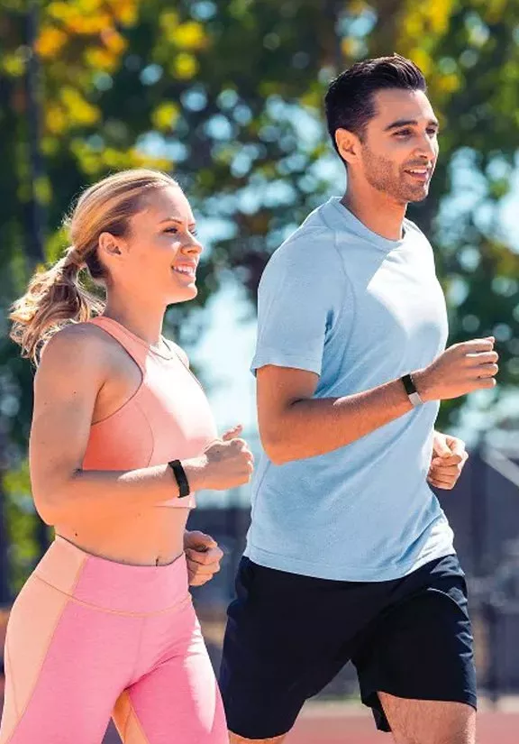 Couple jogging outdoors in sunny park wearing fitness trackers