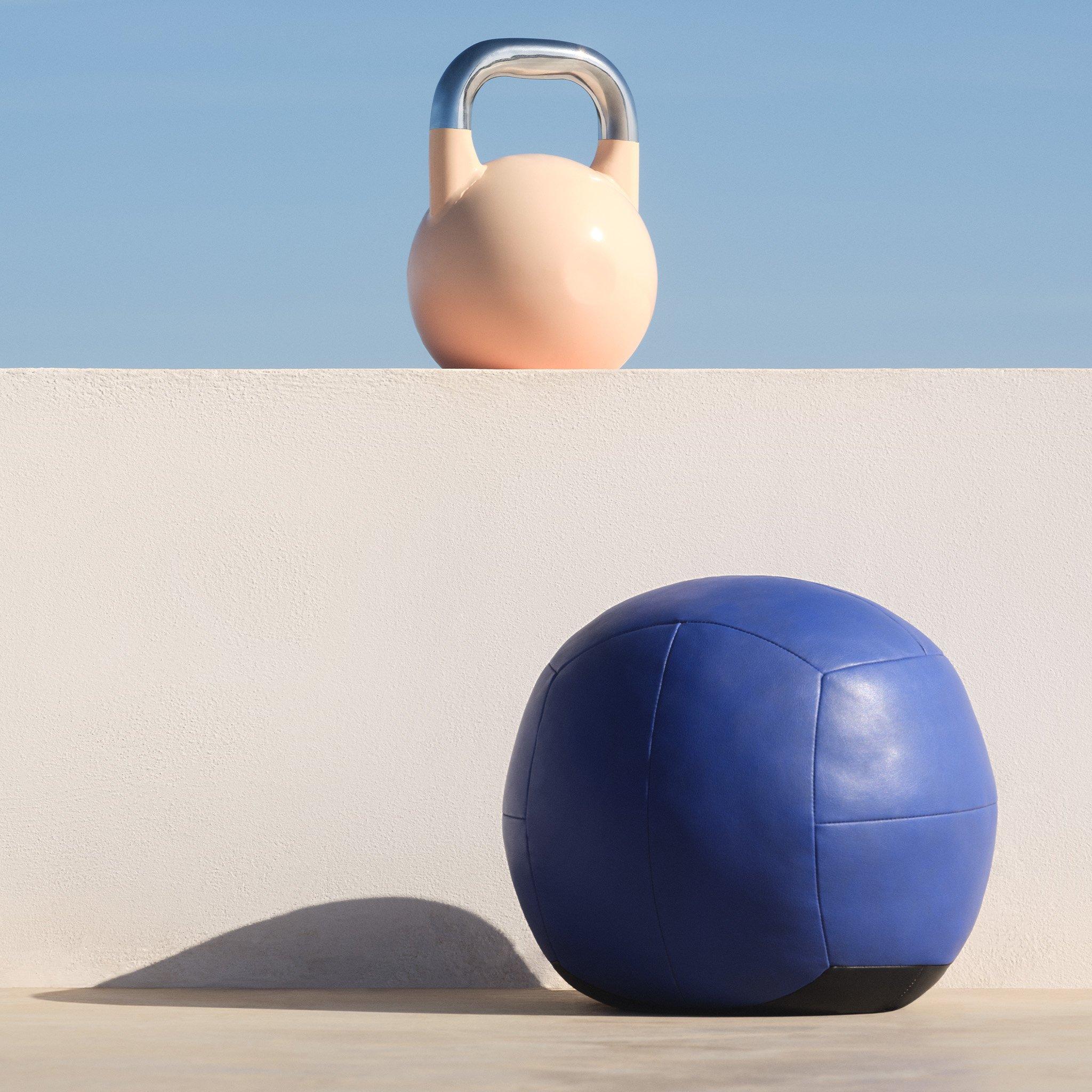 Minimalist fitness setup with a pastel kettlebell and a blue medicine ball against a clean, white backdrop and clear sky.